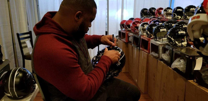 Athlete signing a football helmet with a paint pen at a signing table